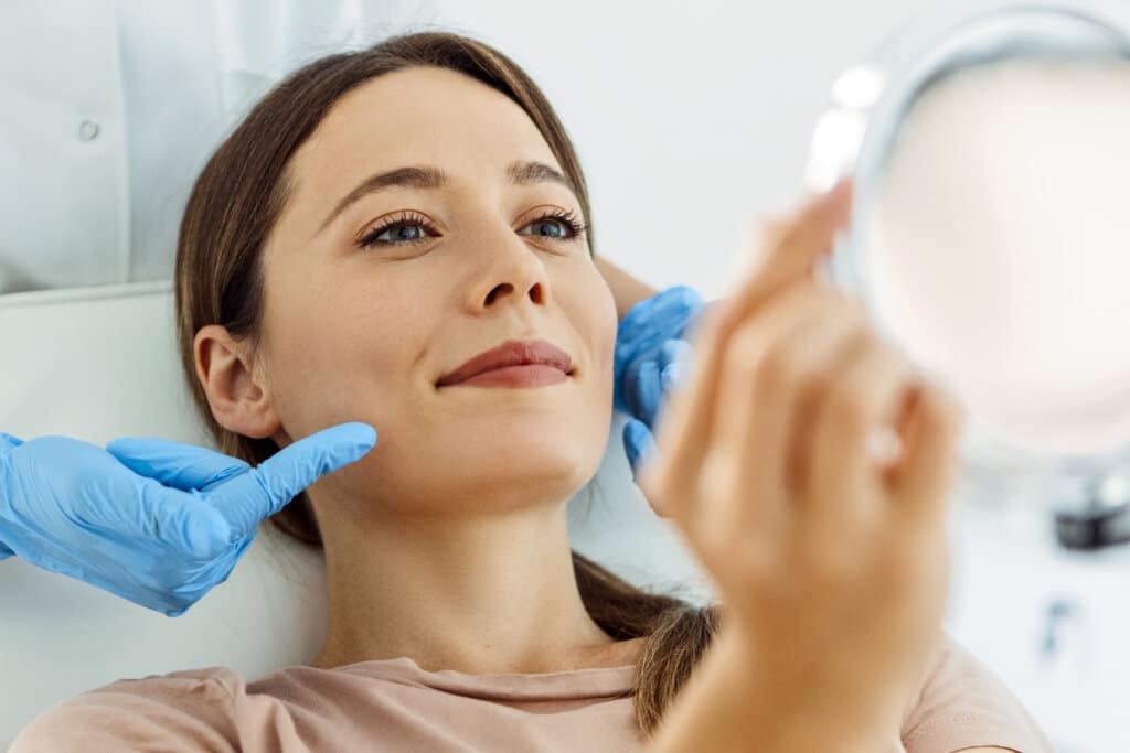 Woman looking at her face in a mirror after having a beauty treatment in a clinic.